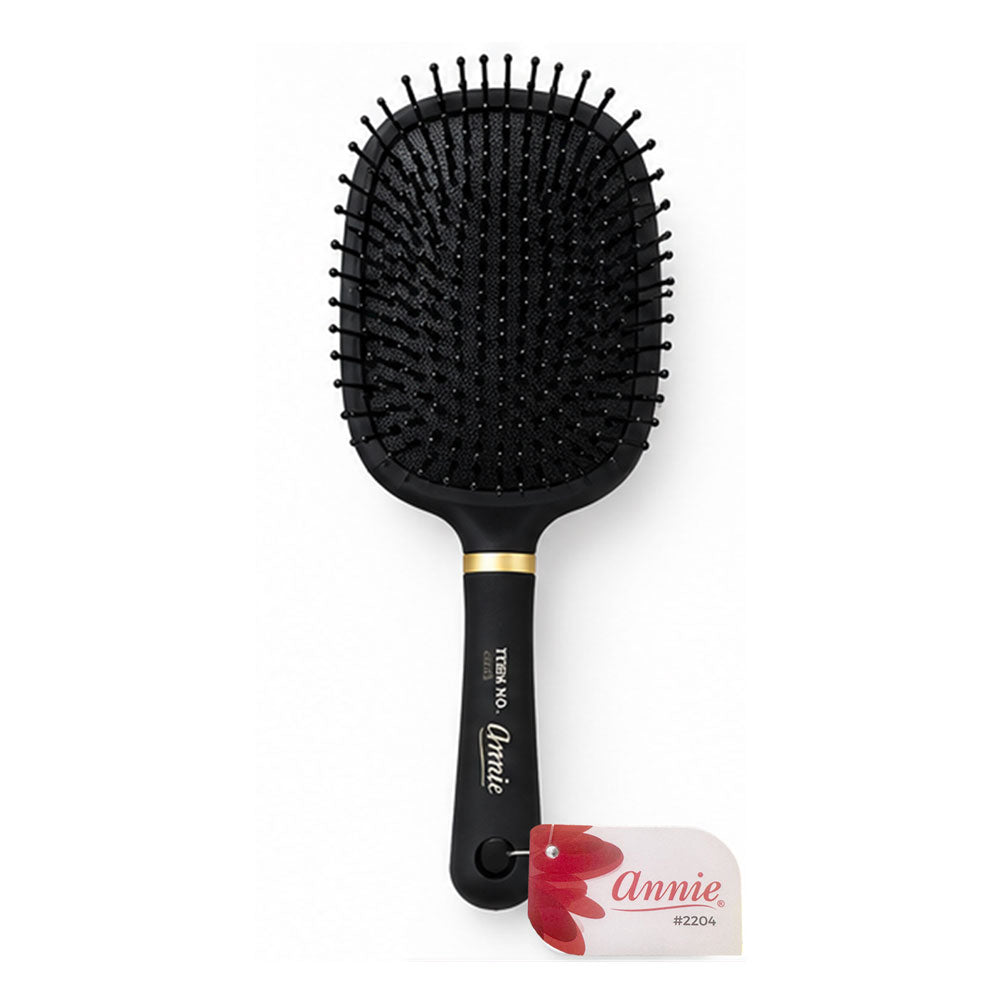 Annie hairbrush with a black paddle head and handle, accented by a gold band near the base of the handle, shown on a white background with a branded hangtag.